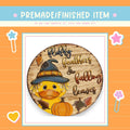 a wooden sign with a duck wearing a witch's hat and holding a pumpkin, surrounded by autumn leaves.