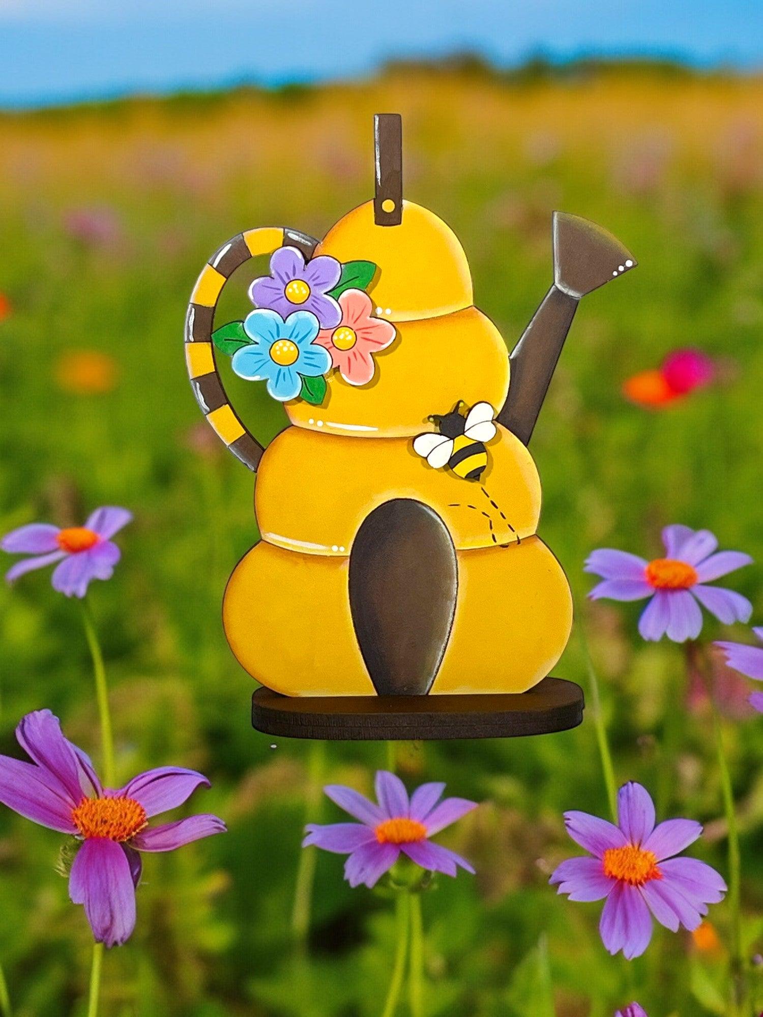 a yellow teapot with a flower on it in a field of purple flowers