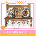 The image is a colorful and vibrant DIY wood paint kit, featuring a wooden bench with various decorative elements such as flowers and birds. The kit appears to be a creative and fun project for those interested in woodworking and painting.