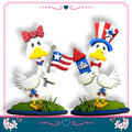 two cartoon ducks holding American flags and a firework, standing on a grassy surface.