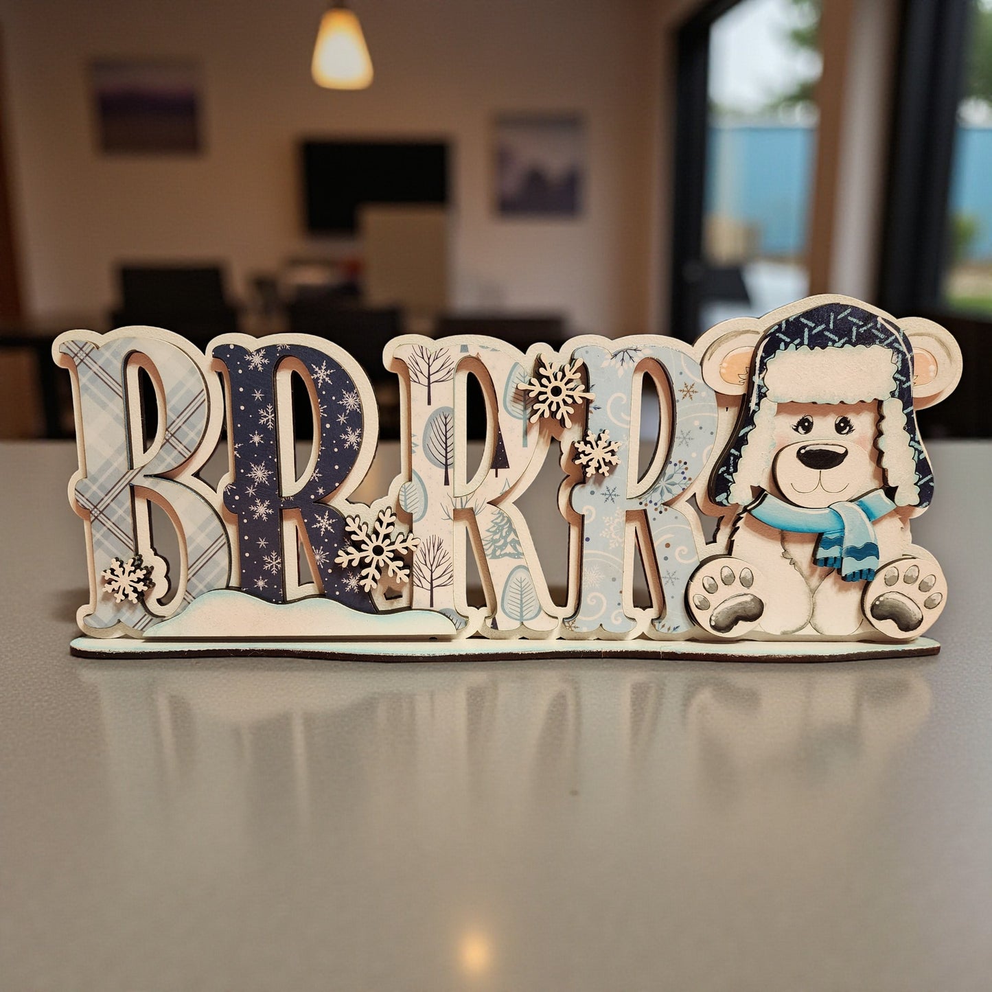 A wooden sign with the word "BRRRR" in large letters, featuring a teddy bear wearing a winter hat and scarf.