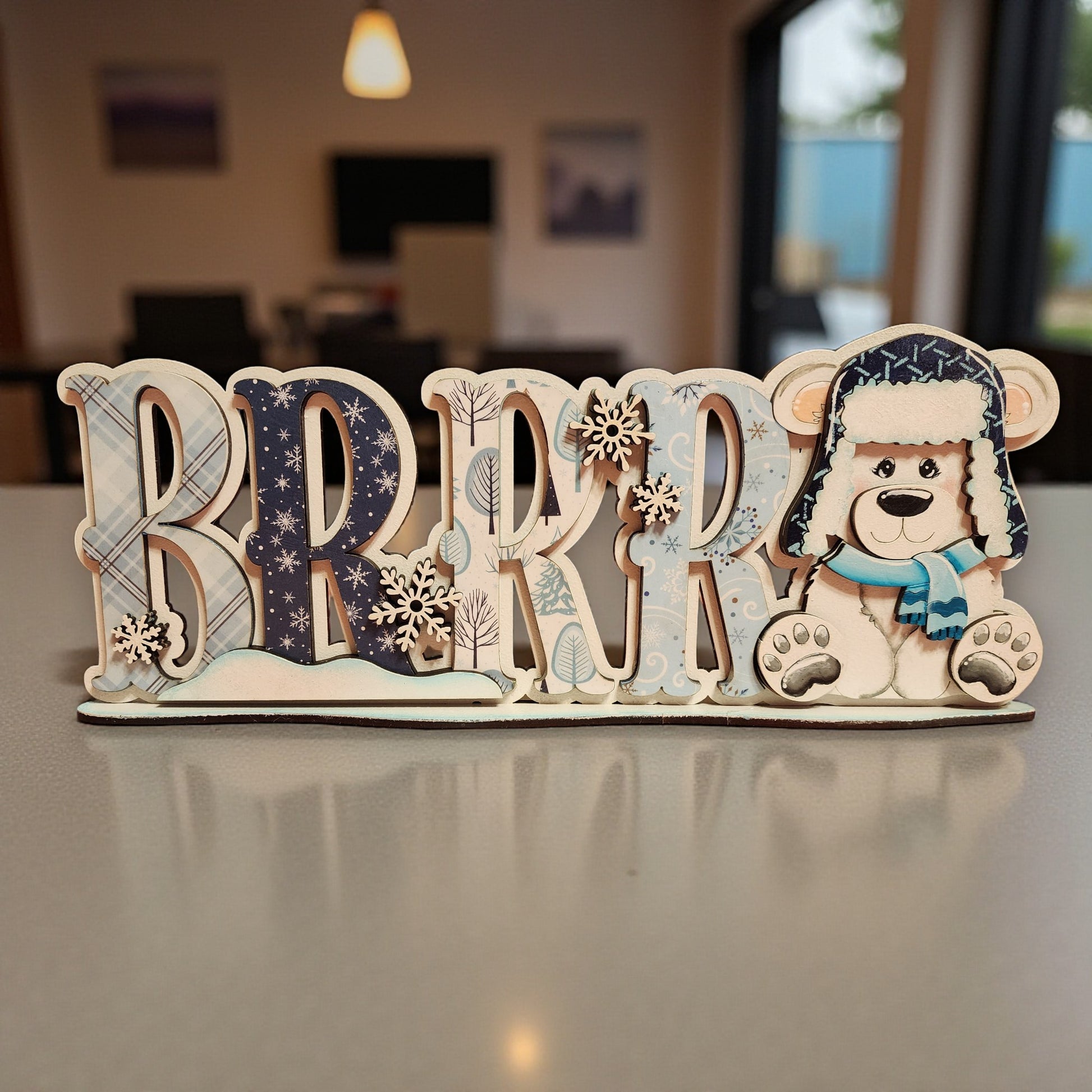 A wooden sign with the word "BRRRR" in large letters, featuring a teddy bear wearing a winter hat and scarf.