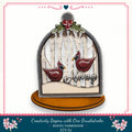 A decorative birdhouse with a snowy winter scene inside, featuring two red birds. The birdhouse is mounted on a wooden base and has a decorative border.