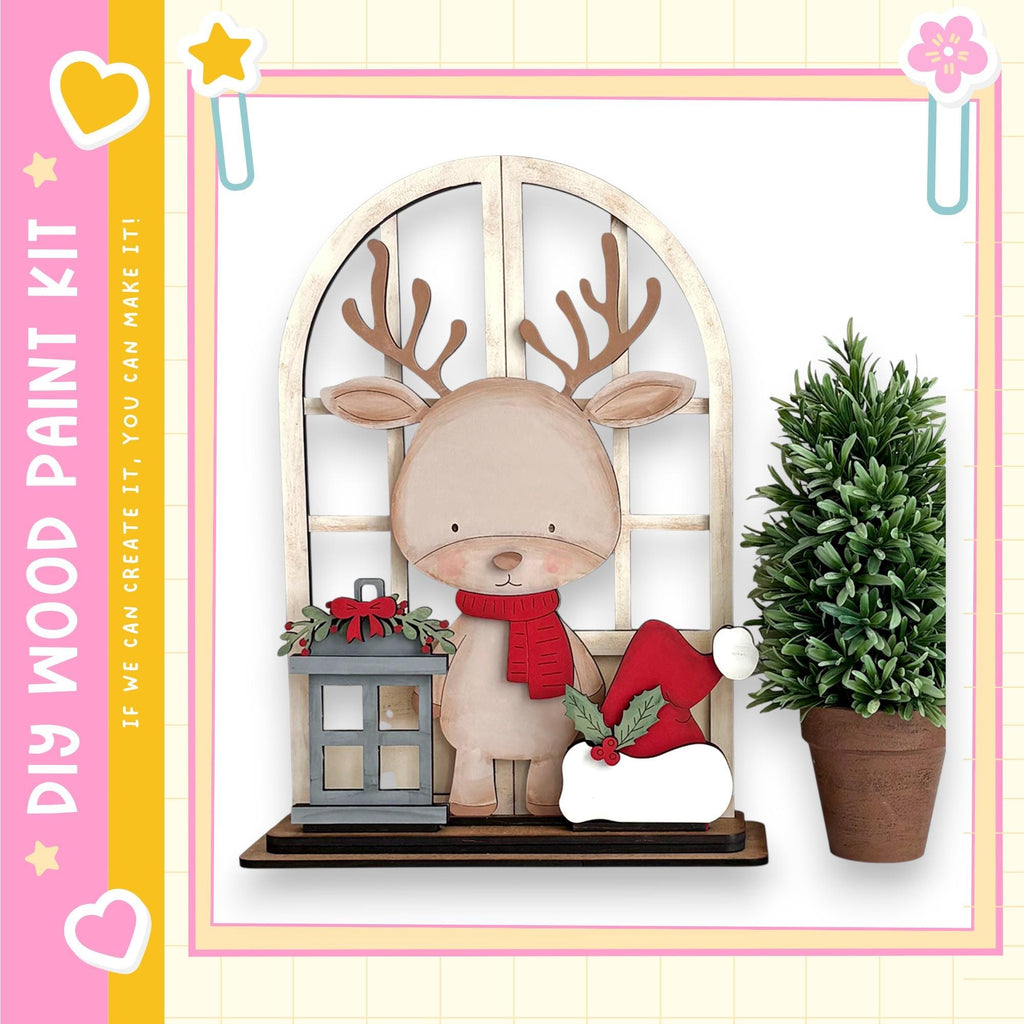 A wooden deer figurine wearing a red scarf and hat stands on a shelf next to a potted plant, with a lantern and star decoration nearby.