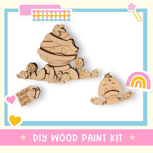 The image is a DIY wood paint kit featuring two wooden characters, one larger and one smaller, with a heart and a rainbow-colored object in the background.