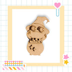 A wooden toy resembling a small, cartoonish creature with a pointed hat and star-shaped cutouts on its body, set against a grid background with various colorful stickers and a heart-shaped object.