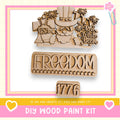 The image is a promotional image for a DIY wood paint kit, featuring a wooden cutout of a U.S. flag and the word "FREEDOM" along with the number "1776".
