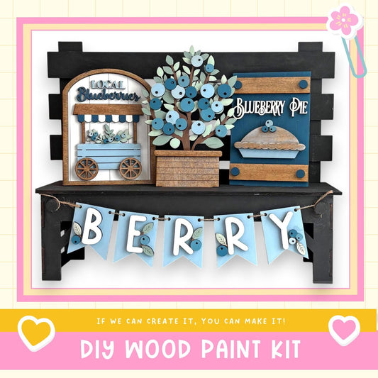 The image is a DIY wood paint kit for creating a berry-themed display, featuring a wooden sign, a wooden wagon, and a wooden pie.