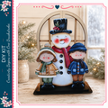 A wooden snowman figure with two children standing beside it, set against a backdrop of a window and pine trees.