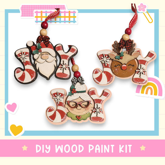 three wooden ornaments hanging from a string, each with a unique design and color scheme. The ornaments include a Santa Claus figure, a reindeer, and a smiling woman with glasses. The background of the image is white, and there is a pink banner at the bottom that reads "DIY WOOD PAINT KIT".