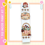 The image is a colorful and whimsical painting kit featuring a wooden frame with various decorative elements such as a mushroom, flowers, and ladybugs. The kit appears to be designed for creating a picnic scene, with the words "Lives a Picnic" and "If we can create it, we can make it" written on it.