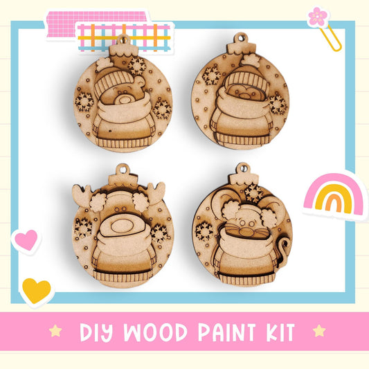The image is a DIY wood paint kit featuring four wooden ornaments with various designs, including a reindeer, a cat, a snowman, and a rainbow.