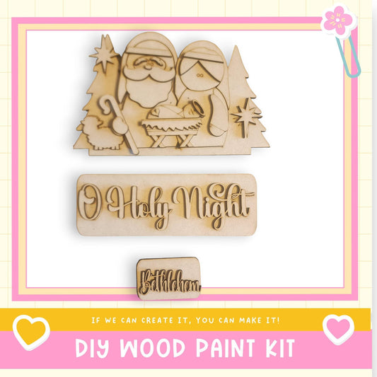 The image is a promotional image for a DIY wood paint kit, featuring a wooden nativity scene with Santa Claus, Mary, and baby Jesus. The kit is designed to allow users to create their own wooden nativity scenes.