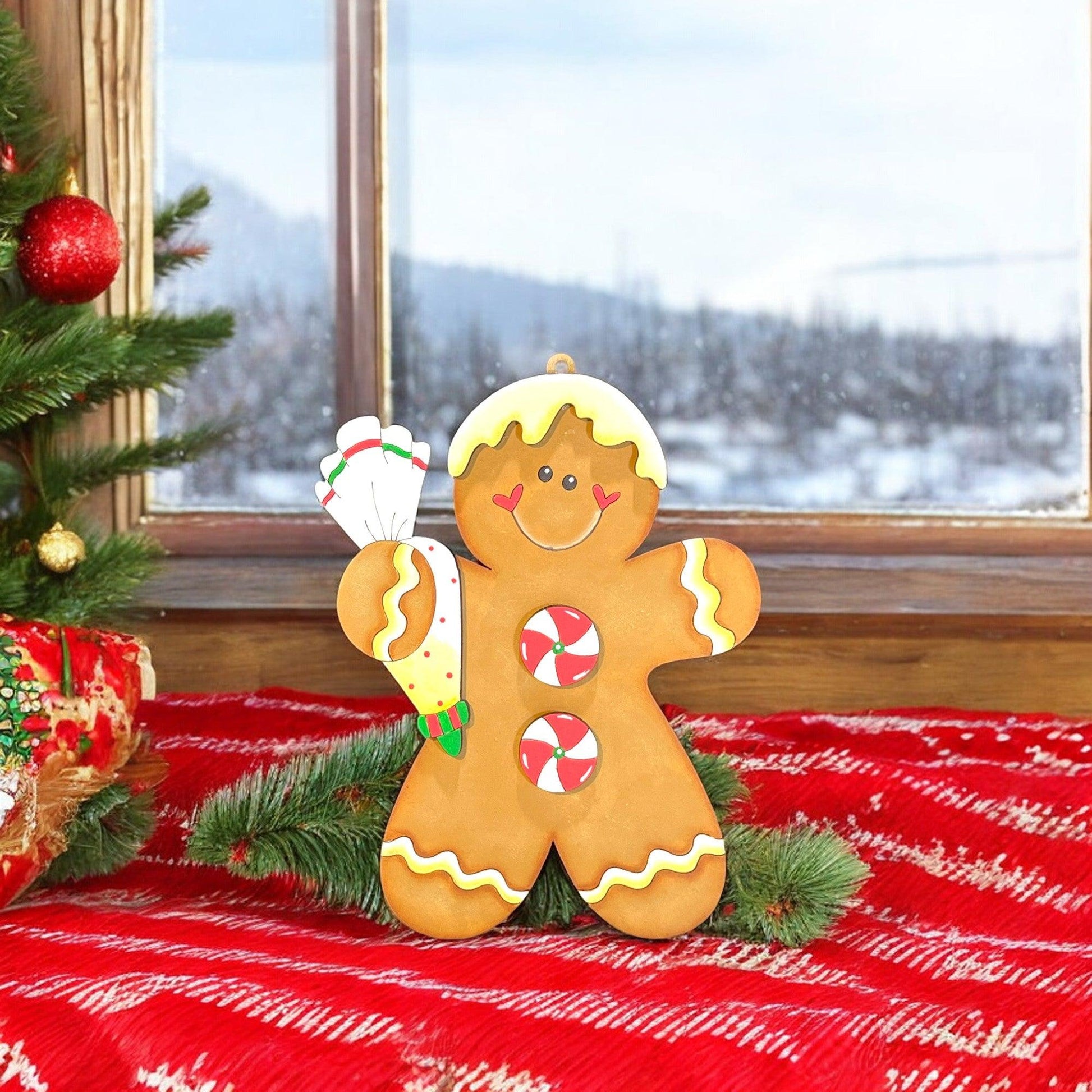 a gingerbread man holding a candy cane next to a christmas tree