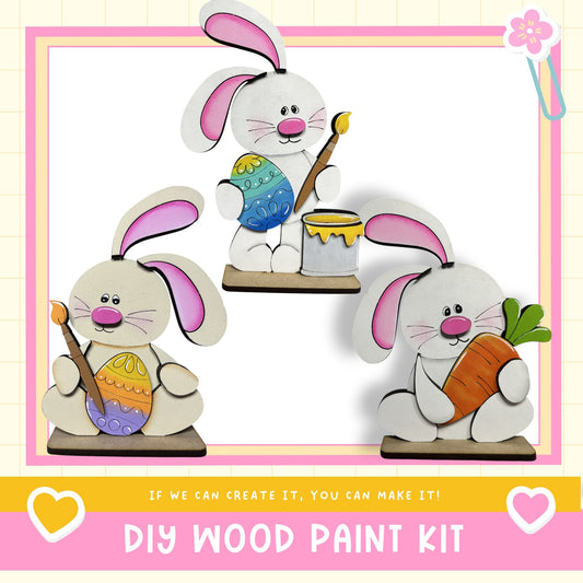 The image is a collage of three wooden Easter bunny figures, each holding a different Easter egg. The text below the image reads "DIY WOOD PAINT KIT" and "If we can create it, you can make it!"