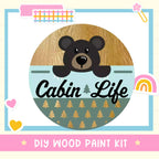 The image is a colorful and whimsical illustration featuring a bear's head peeking out from behind a wooden frame, surrounded by various decorative elements such as hearts, rainbows, and stars.