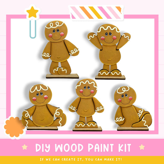 a DIY wood paint kit for creating wooden gingerbread man figures. There are five gingerbread man figures in various poses, including sitting, standing, and kneeling, all with white icing and a smile. The kit appears to be made of wood and includes instructions for painting the figures.