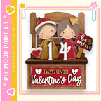 A wooden bench with two cartoon figures, one wearing a red hat and the other a red dress, sitting on it. The bench has a sign that says "14 DAYS UNTIL Valentine's Day".
