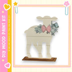 A wooden sheep figurine with a bow on its head, standing on a wooden base.