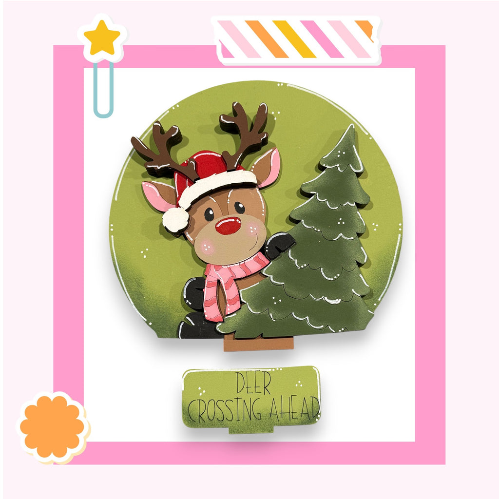 A cartoon reindeer wearing a Santa hat and scarf is holding a Christmas tree, with the text "DEER CROSSING AHEAD" below the tree.