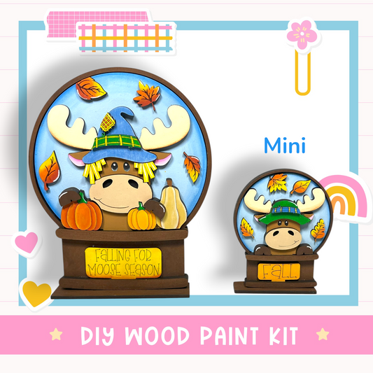a DIY wood paint kit for creating a wooden snow globe with a moose wearing a witch's hat and surrounded by autumn leaves.