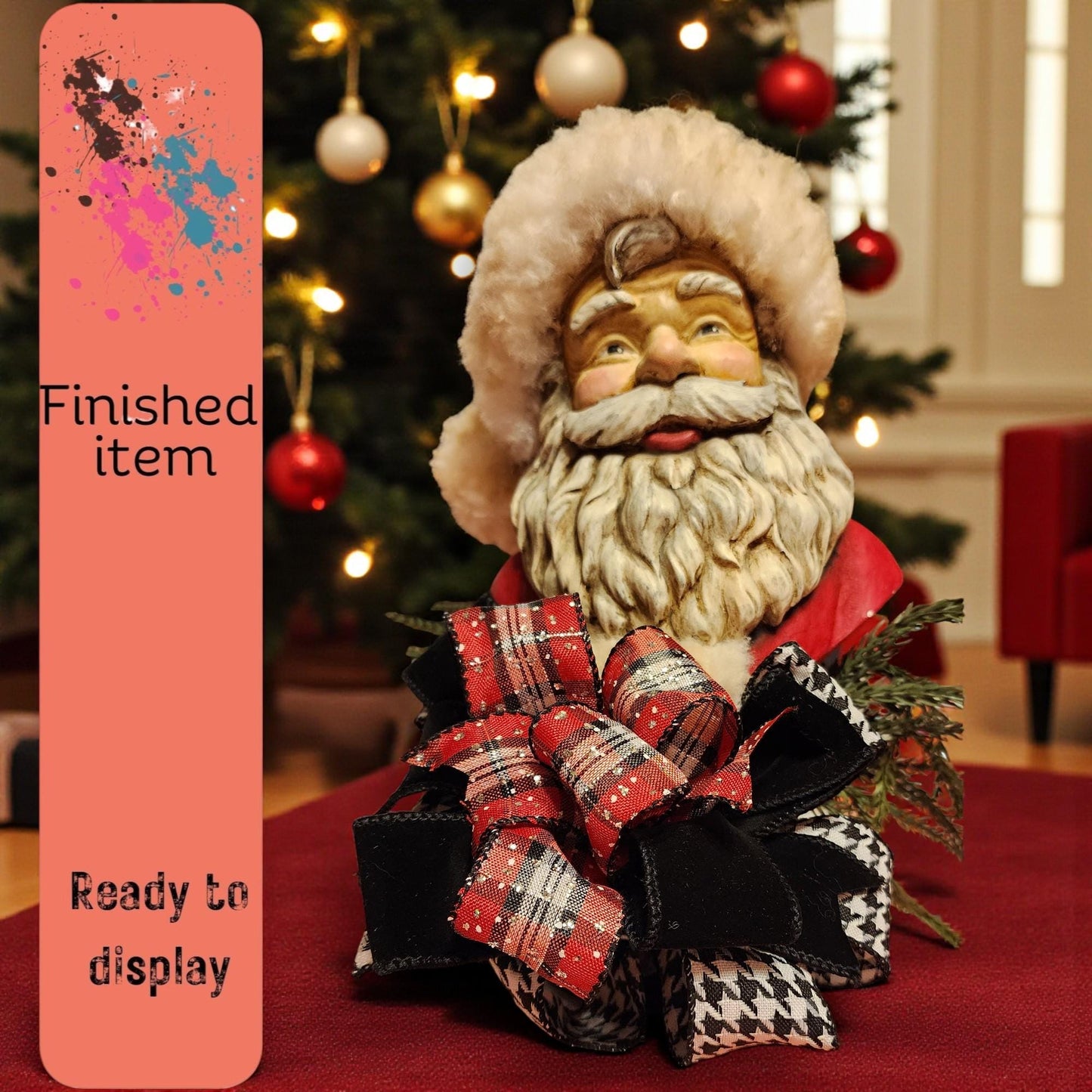 A Santa Claus figurine with a red bow sits on a table, with a Christmas tree and ornaments in the background.