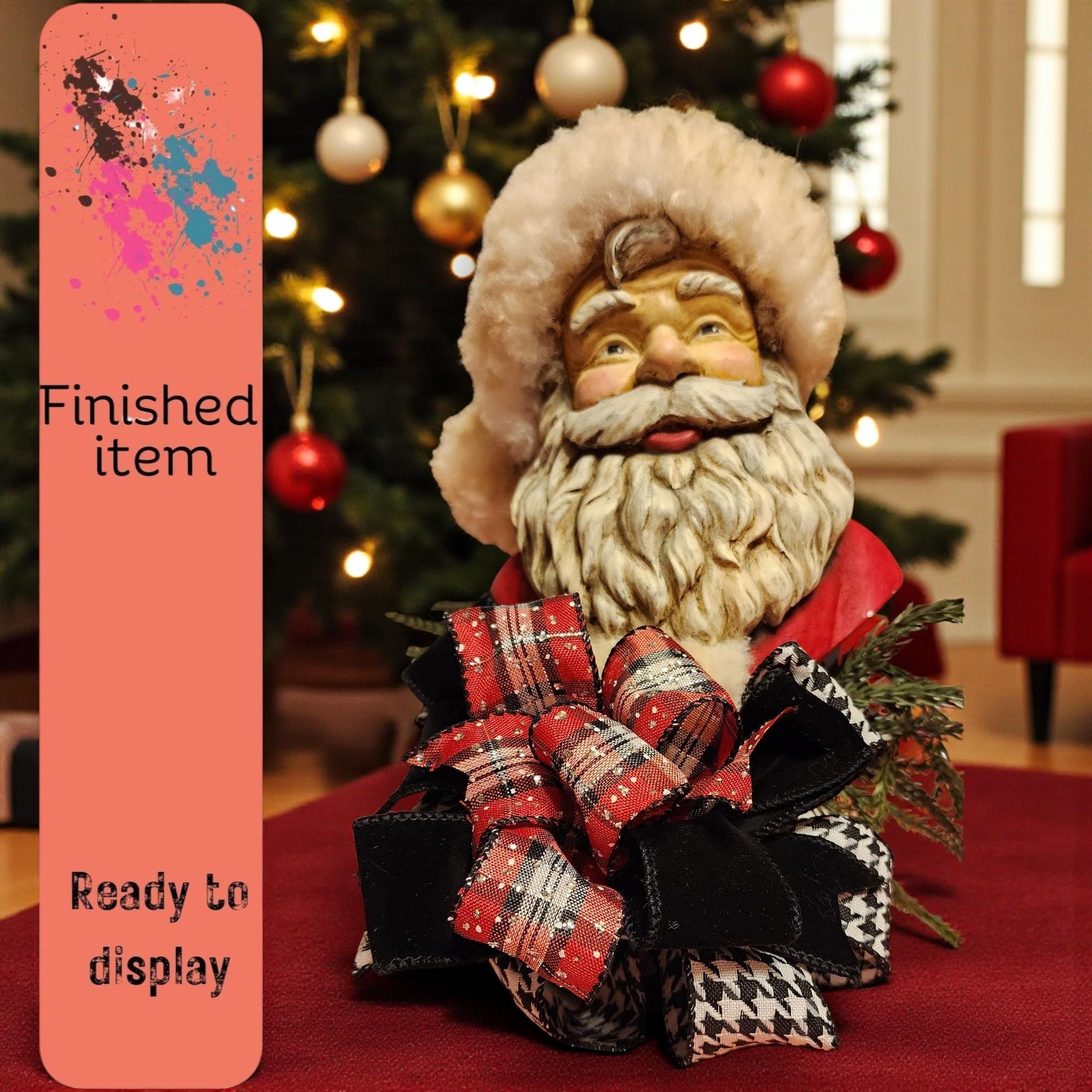 A Santa Claus figurine with a red bow sits on a table, with a Christmas tree and ornaments in the background.