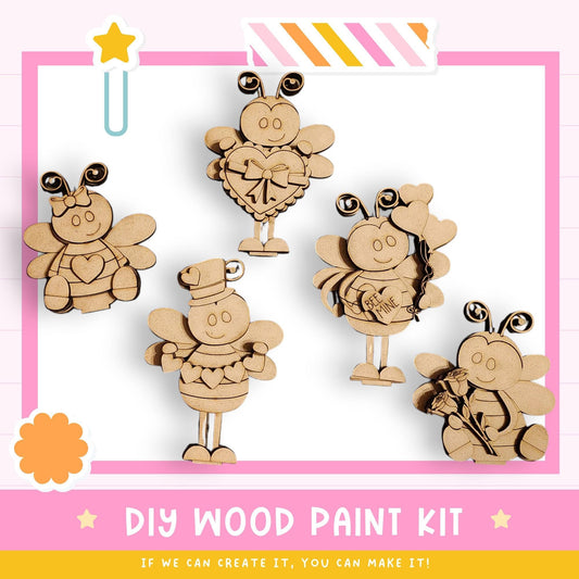 The image is a DIY wood paint kit featuring five wooden bee characters in various poses, including one holding a heart and another holding a bouquet of flowers. The kit appears to be made of wood and is designed for painting.