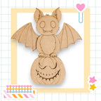 A wooden bat with a carved face is perched on a carved pumpkin, surrounded by colorful stickers and a heart-shaped object.