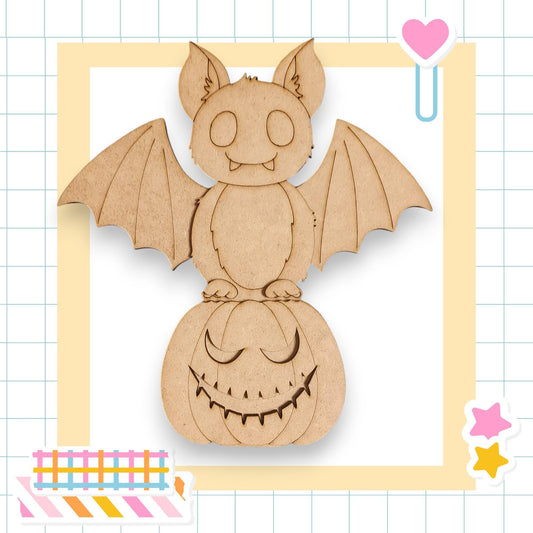 A wooden bat with a carved face is perched on a carved pumpkin, surrounded by colorful stickers and a heart-shaped object.