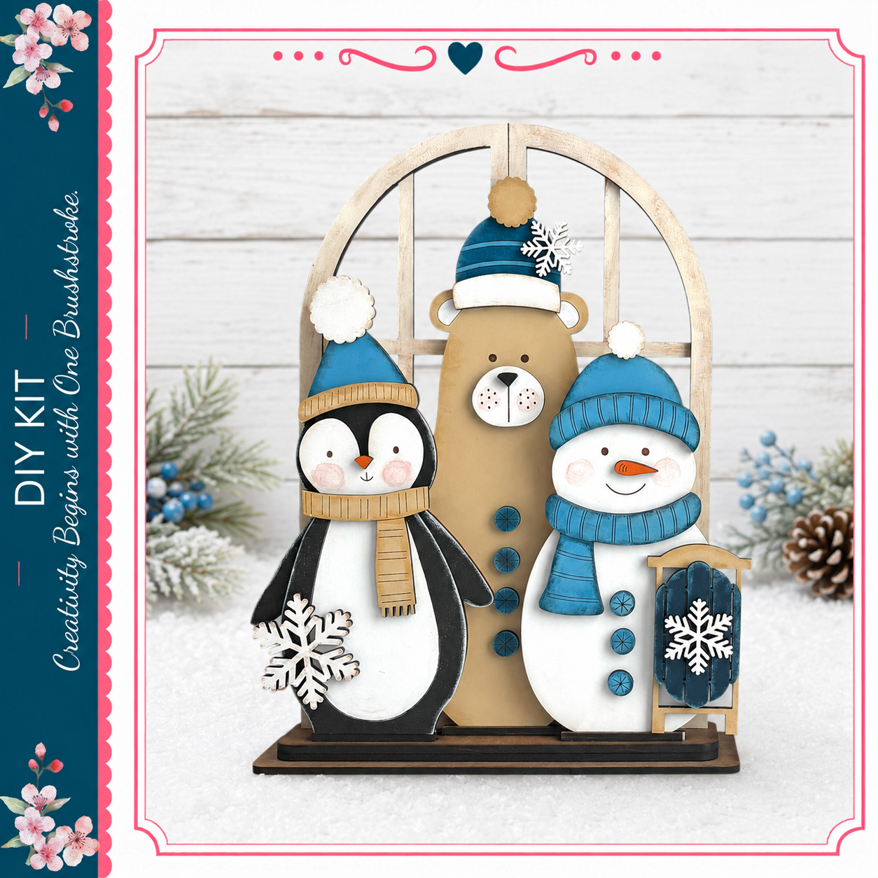 A wooden cutout of a penguin, a teddy bear, and a snowman, all wearing winter hats and scarves, is displayed on a wooden stand against a snowy background.