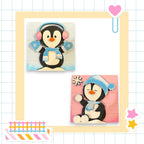 The image is a collage featuring two cute penguin illustrations, one standing and one sitting, both wearing winter accessories like mittens and hats.