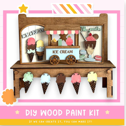 A wooden ice cream stand with various ice cream flavors displayed on cones, along with a sign that reads "ICE CREAM". The stand is made of wood and has a pink and white striped border. The image also includes a DIY wood paint kit and a statement encouraging creativity.