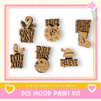 a DIY wood paint kit with various wooden ornaments and decorations, including a candy cane, peace sign, jingle bells, holly, Santa hat, and a "believe" sign.
