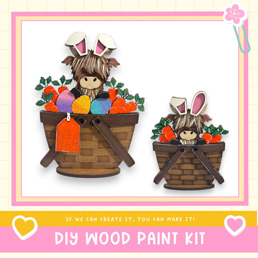 two wooden baskets filled with Easter eggs and carrots, each with a small bunny wearing a pair of bunny ears. The baskets are placed on a white background, and there is text at the bottom of the image that reads "DIY WOOD PAINT KIT" and "IF WE CAN CREATE IT, YOU CAN MAKE IT!"