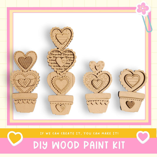 a DIY wood paint kit with four heart-shaped cutouts arranged in a row, each in a pot. The kit appears to be made of cardboard and is designed for creating wooden heart-shaped decorations or ornaments.
