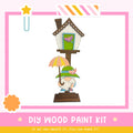 a wooden birdhouse with a gnome holding an umbrella, set against a pink and white background.