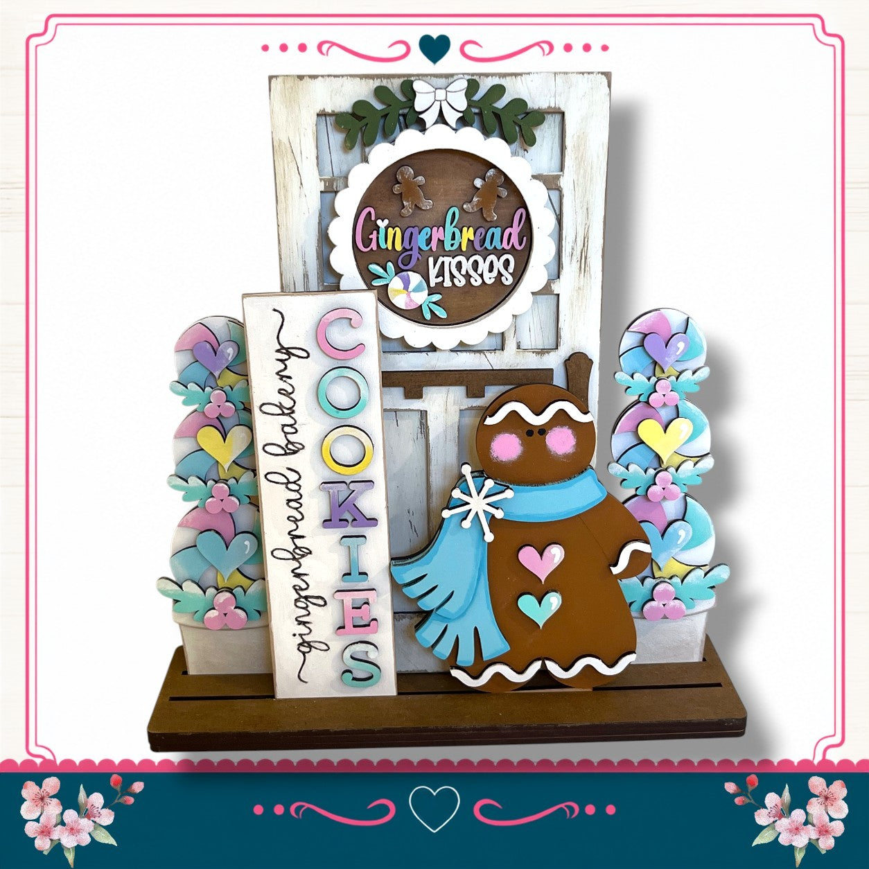A gingerbread house-themed display with a gingerbread cookie, a sign that says "Gingerbread", and a wreath. The display is set against a white background with a pink border.