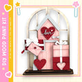 The image is a wooden paint kit featuring a pink wooden door with a heart-shaped window, decorated with a pink heart, a pink envelope, and a pink gift box.