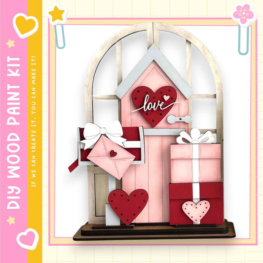 The image is a wooden paint kit featuring a pink wooden door with a heart-shaped window, decorated with a pink heart, a pink envelope, and a pink gift box.
