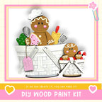 A DIY wood paint kit featuring a gingerbread man and a small child, along with various craft supplies, such as a paintbrush and a palette, all set against a pink and white background.