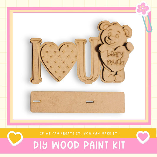 The image is a DIY wood paint kit featuring a wooden heart-shaped sign with the word "I love you" written on it, and a wooden bear figure holding a heart-shaped sign that says "bear much".