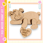 A wooden bear figure with a heart-shaped message attached to it, set against a pink and yellow background.