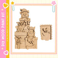 A wooden paint kit featuring a playful scene of dogs wearing hats and holding presents, with a pink and yellow border.