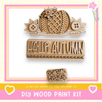 The image is a DIY wood paint kit featuring a wooden sign with the word "Hello Autumn" and a wooden cutout of a flower. The kit appears to be made of wood and is designed for creating custom signs and decorations.