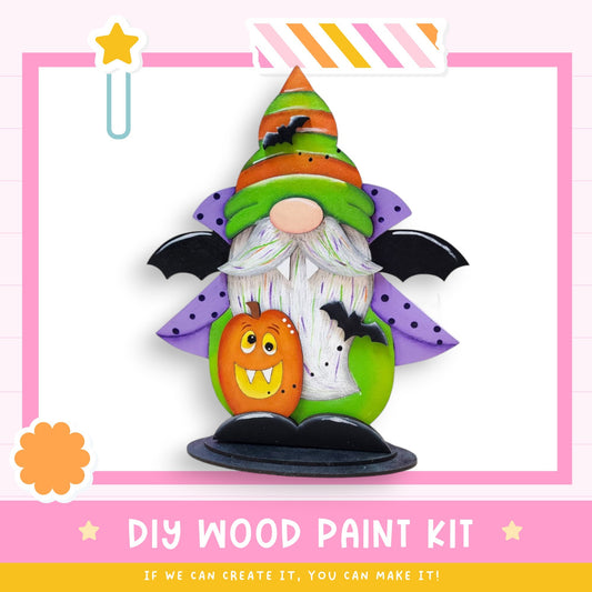 a DIY wood paint kit for creating a Halloween-themed decoration, including a gnome-like figure with a bat-like hat, a carved pumpkin, and a star.