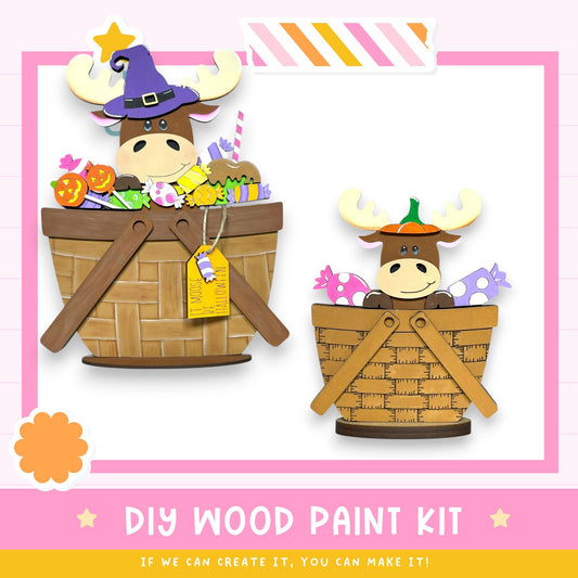 two wooden baskets, each containing a moose wearing a witch's hat. The baskets are filled with various Halloween-themed items, such as candy and pumpkins. The image also includes text that reads "DIY WOOD PAINT KIT" and "IF WE CAN CREATE IT, YOU CAN MAKE IT!"