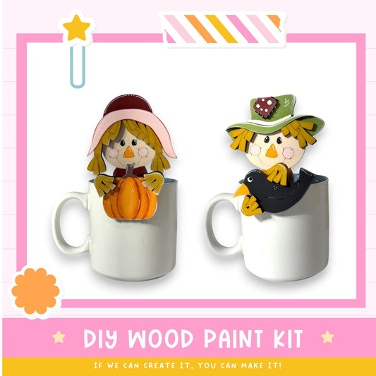 two ceramic mugs with wooden scarecrow figures painted on them, along with a DIY wood paint kit and a star decoration.