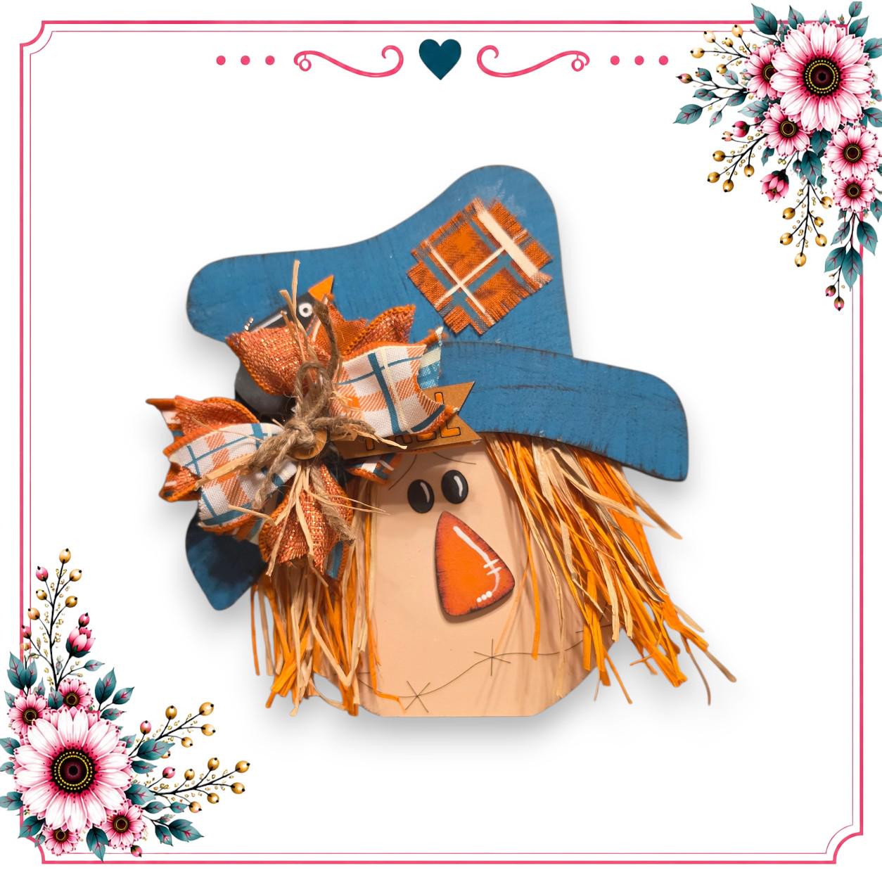 A wooden scarecrow with a blue hat and orange accents, surrounded by colorful floral decorations.