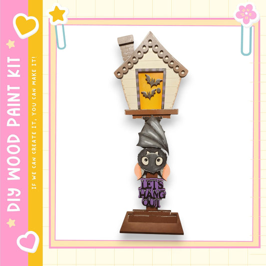 A Halloween-themed wooden paint kit featuring a bat-shaped house decoration with a sign that says "Let's hang out".